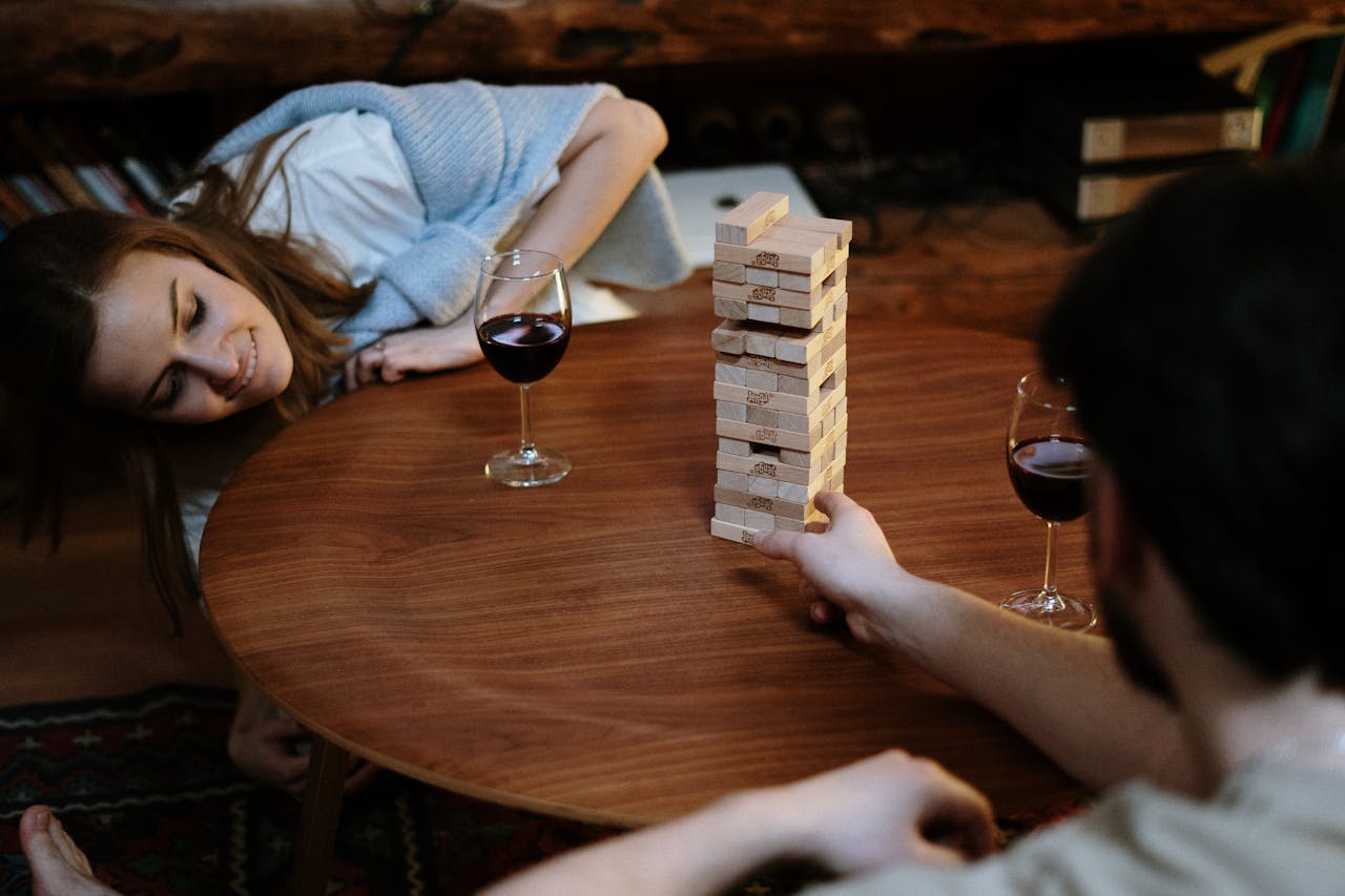 A couple enjoying a cozy evening playing Jenga with glasses of red wine at home.